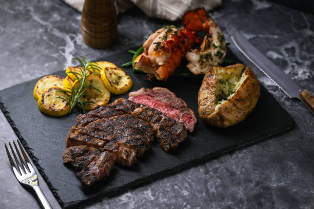 surf and turf, ribeye steak and lobster tail on black marble background - surf and turf prepared shrimp steak grilled стоковые фото и изображения