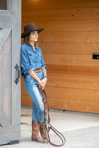 Cowgirl leans against barn door and looks off