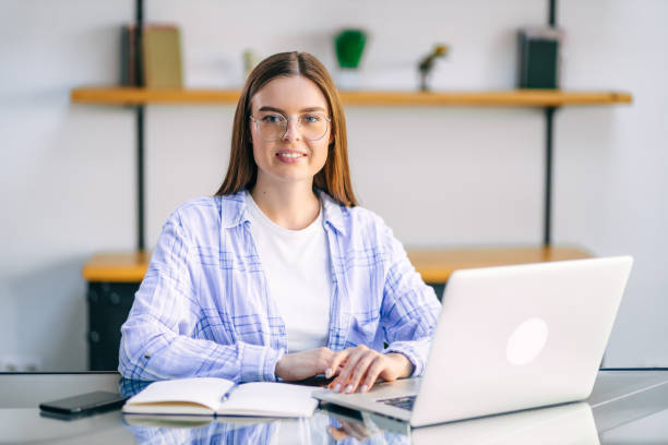 istock Young woman sitting at table at home working using laptop computer with happy face with confident smile. 1930972262