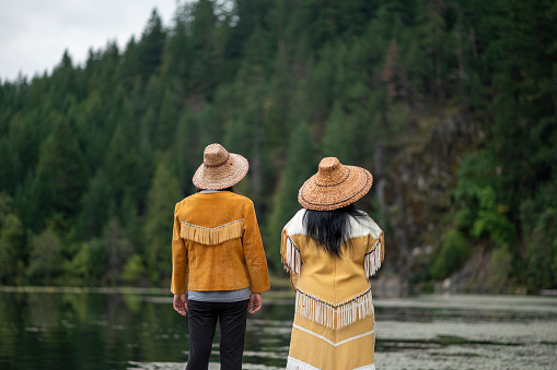 Indigenous women wearing traditional outfits stand on pier and enjoy lake together