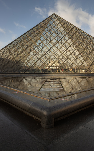 France, Paris - Jan 03, 2024 - At the front of Famous Louvre Museum and its grand glass pyramid during day time with water reflection effect by after raining. is one of the world's largest museums in Paris, Space for text, Selective focus.