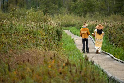 Indigenous women wearing traditional outfits walks down boardwalk over marsh together