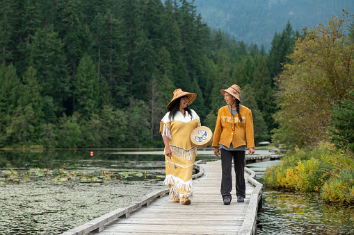 Indigenous women wearing traditional outfits walks down boardwalk over marsh together