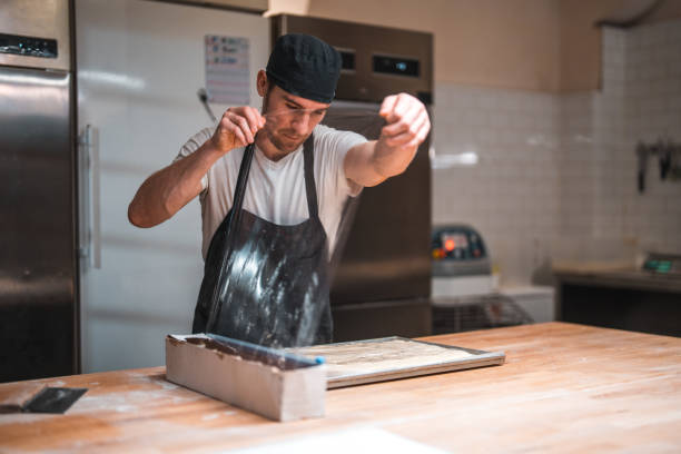 istock Caucasian Male Baker Wrapping Dough In A Plastic Foil In An Artisan Bakery 1930987980