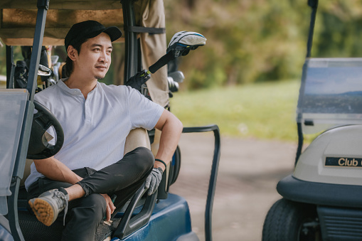 Asian Chinese golfer sitting on golf cart resting looking away smiling leg crossed