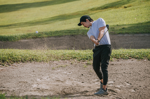 Asian chinese male golfer hitting the ball at sand bunker