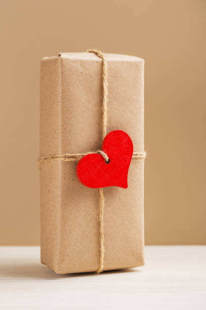 istock Craft gift box with wooden heart on a light wooden table. Eco-friendly concept. Rustic style. Romantic concept for presents. Vertical orientation. 1931045356