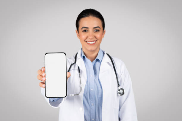 istock Happy latin female doctor shows cellphone with blank screen in studio 1931079162