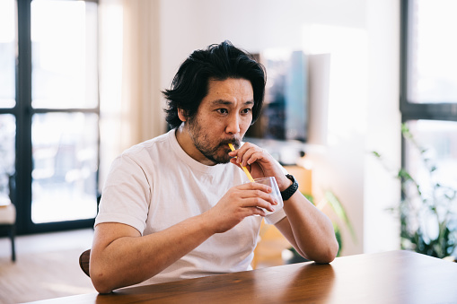 Dentin hypersensitivity. Japanese man in his forties uses a straw to drink water, showcasing a considerate way to bypass tooth sensitivity and enjoy a refreshing beverage