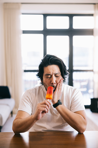 Dentin hypersensitivity. Japanese man dealing with a toothache brought on by enjoying the frozen delight of an ice popsicle