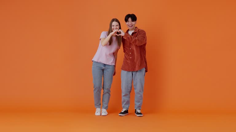 Joyful European woman and Asian man show heart shapes