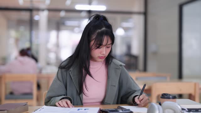 Asian female student is studying and comprehending study materials she learned at the Co-Working Space. Active learning session with focused understanding.