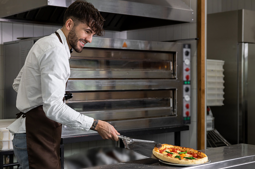 Smiling cooker preparing tasty pizza in pizzeria