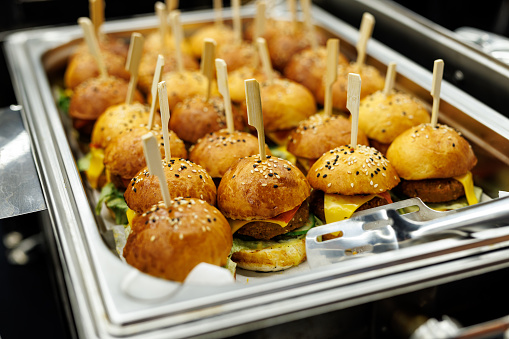 A platter of savory mini burgers with toothpicks and condiments.