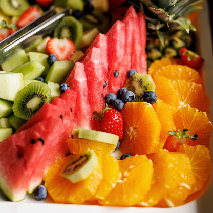 A vibrant fruit platter with watermelon, kiwi, strawberries, blueberries, and oranges on a white dish.