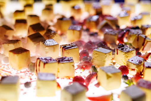 The set of bite-sized small cheesecakes on a white surface. The steam, berries, sugar powder, and chocolate are used as decor