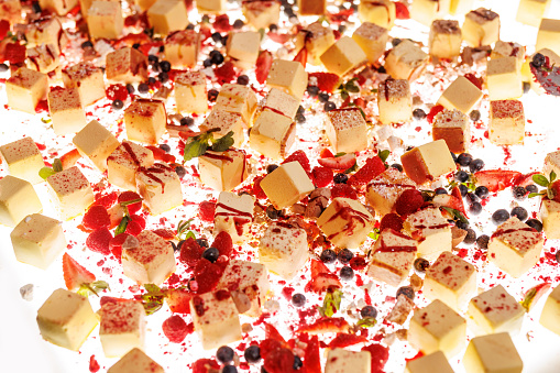 The set of bite-sized small cheesecakes on a white surface. Berries, sugar powder, and chocolate are used as decor