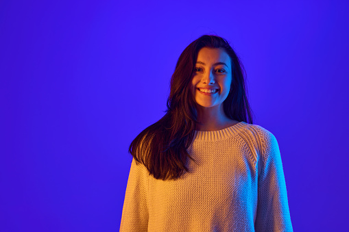 Eye Contact. Portrait of young girl looks directly at the camera, establishing strong connection with viewer against gradient blue background. Concept of positive emotions, fashion and beauty. Ad