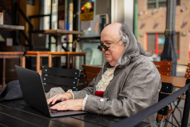 medium close up shot of benjamin franklin impersonator working on his laptop - benjamin franklin history american culture portrait imagens e fotografias de stock