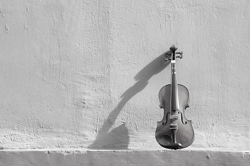 Black and white photo of a violin is placed on the side of an old wall. Suitable as a background image for various design needs, quotes, posters, etc.