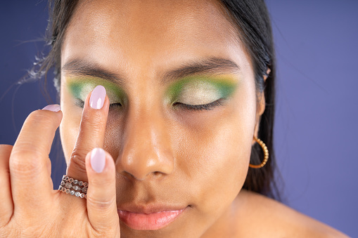 Finger make-up on the eyelids of a young woman, on a purple background.