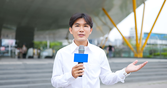 portrait asian male reporter standing in front of metro station building has live broadcast