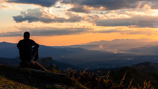 Silhouette of a man sitting on the rock waiting for sunset.