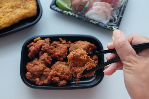 Close-up POV shot unrecognizable person eating a takeout karaage (Japanese Fried Chicken) from a plastic bento box
