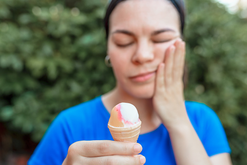 Woman making gesture of dental pain after eating ice cream