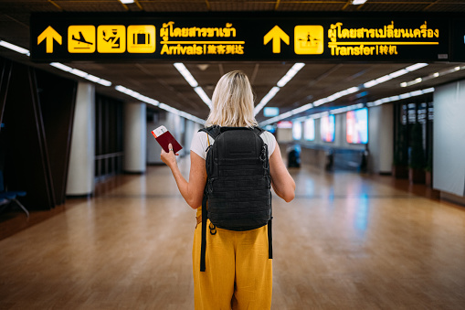 Rear view of a woman at the airport holding a passport with a boarding pass.