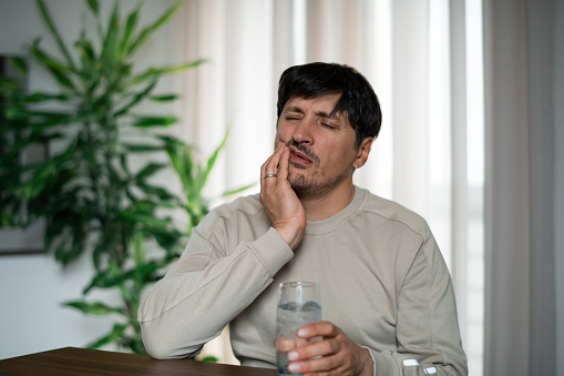 Man at home with cold drink suffering from tooth sensitivity