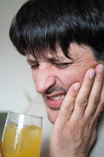 Man at home with cold drink suffering from tooth sensitivity