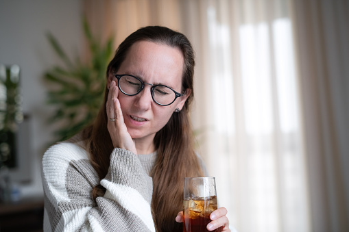 Woman at home with cold drink suffering from tooth sensitivity