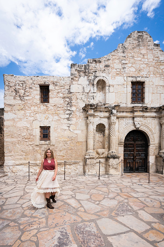 Blond female with long hair and skirt at the exterior entrance of the Alamo site, National Mission Park, San Antonio, Texas, USA