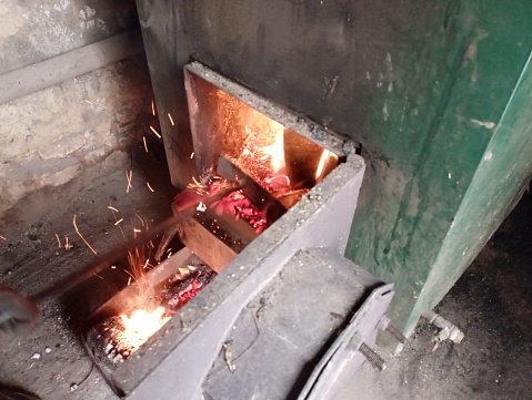 The lower door is open in the green metal cauldron, from which red-hot coals fall out and sparks fly. The topic of heating a house with solid fuel in winter.