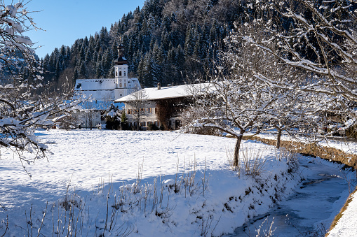 View of the mountaineering village of Sachrang in Chiemgau, Bavaria, Germany in winter.  Frozen stream (Prien) and snow-covered garden in the foreground
