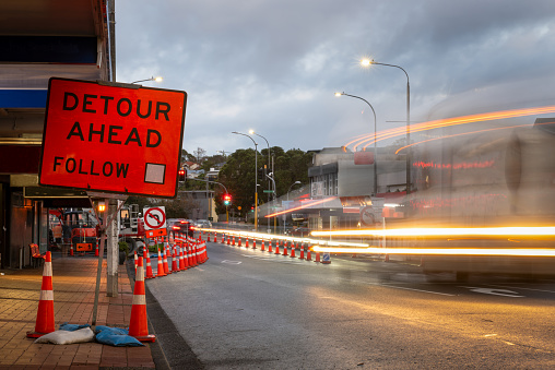 Orange traffic cones on the road. Bus light trails approaching traffic lights. Road works in Auckland.