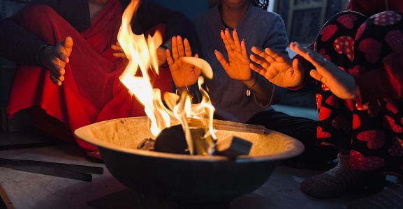 Group of people gathering around a bonfire and warming hands in cold winters at home.