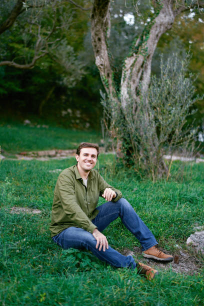 istock Young man sitting on green grass near the tree 1931770205
