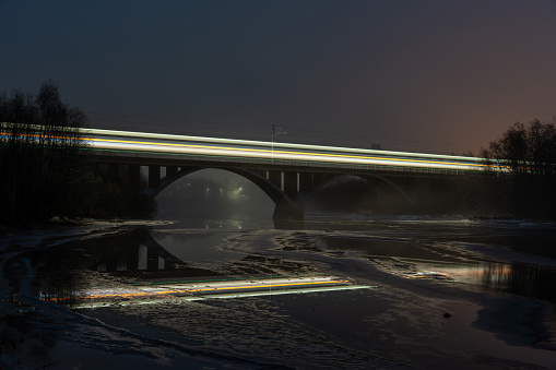 A train on a bridge over dark river with lights reflecting on the water surface