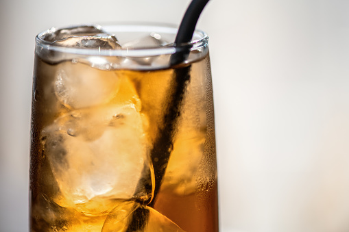 Ice tea or soda with ice cubes and drinking straw indoors