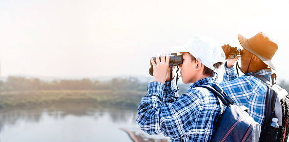 Group of asian schoolboys spending their free times on long weekend in summer season by learning and watching fish, birds, trees, flowers, animals, insects and small creatures by using binoculars, magnifying glasses and compass, soft focus.