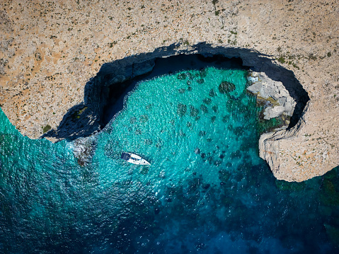 Experience serenity with an aerial view of a boat at Malta's Blue Lagoon, where crystal-clear waters and natural beauty create a mesmerizing scene.