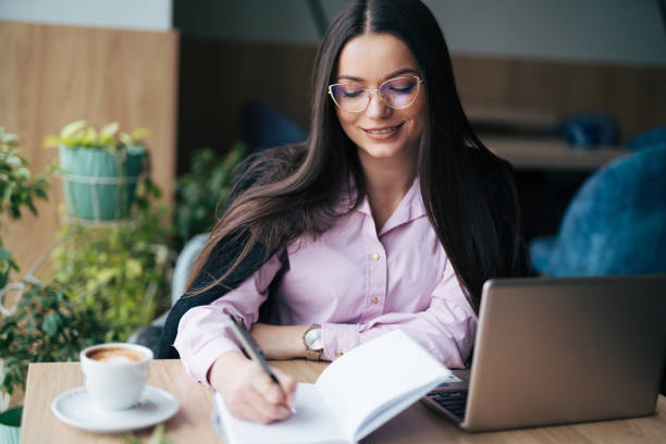 istock Young businesswoman writing notes while using laptop during a meeting in the cafe 1931896600