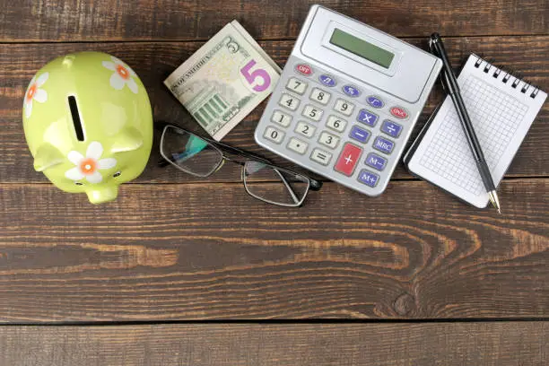 green pig piggy bank money.calculator and notepad on brown wooden table, money saving concept.