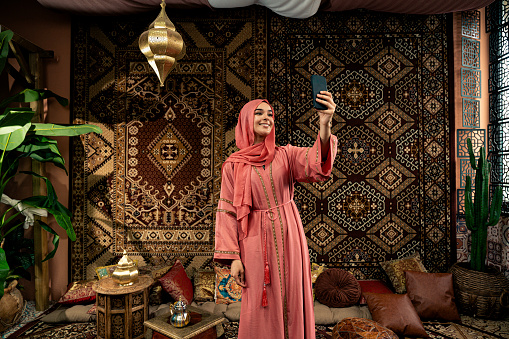 Beautiful young woman wearing colored abaya indoor in an arabian traditional cafe