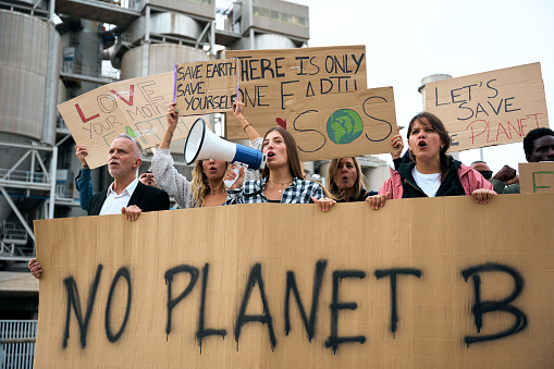 Group diverse people of demonstrators protesting against climate change. Woman shouting with a megaphone banners at a march in favor of the environment.