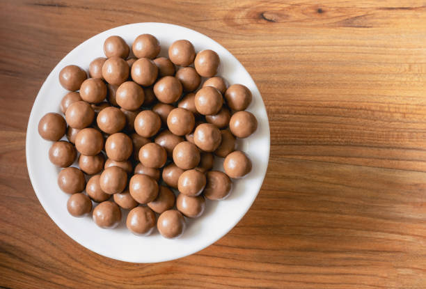 Maltesers milk chocolate balls on a plate on a pine tree surface, top view