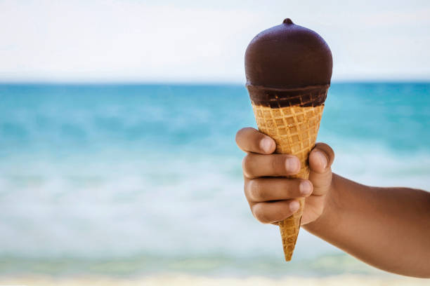 istock Ice Cream Cone in Child Hand on Sea Beach Background 1932001848