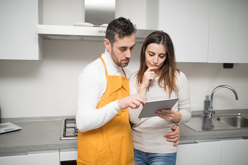 Happy couple looking for a recipe on the tablet to cook in their kitchen